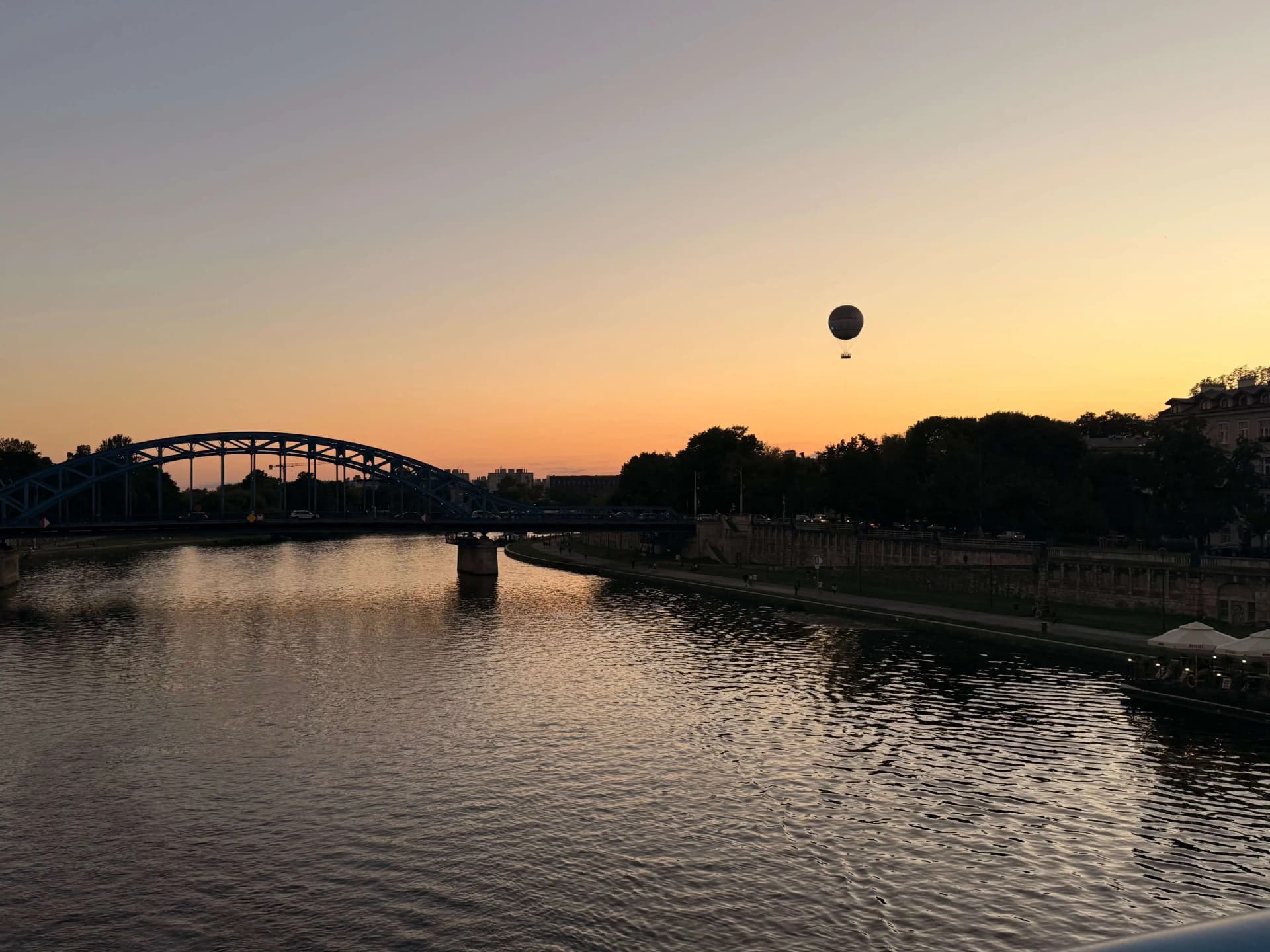 Zdjęcie przedstawia zachód słońca nad rzeką Wisłą w Krakowie, w tle widoczny jest balon oraz most im. Marszałka Józefa Piłsudskiego