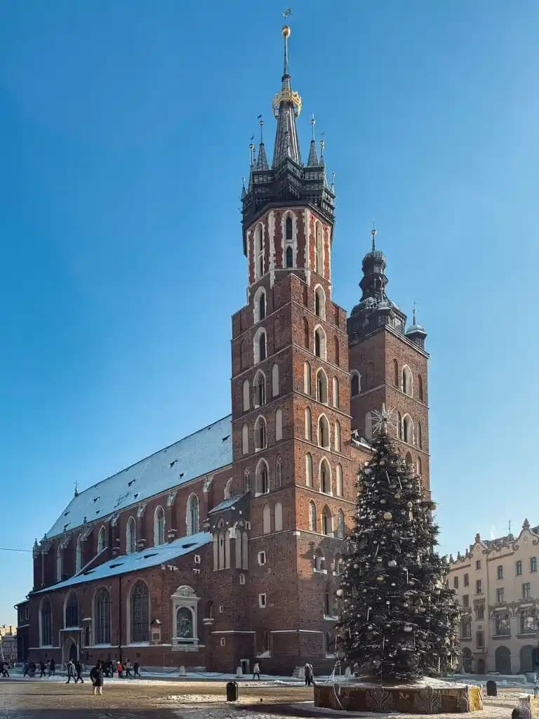 Zdjęcie przedstawia kościół Mariacki w Krakowie widoczny z płyty rynku od lewej strony sukiennic patrząc na katedrę